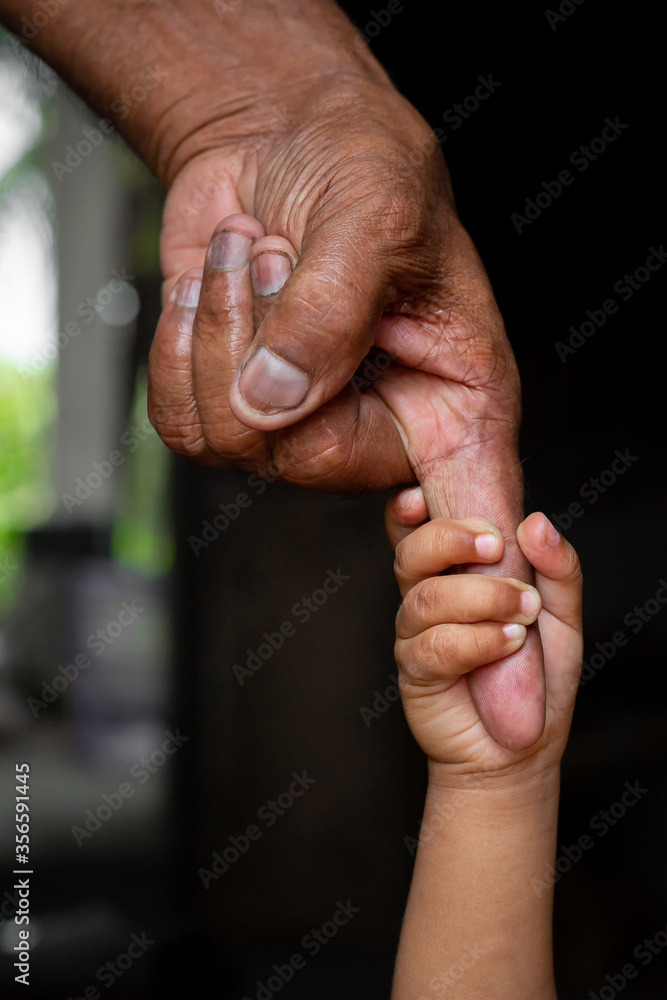 A baby's hands holding tightly A senior man's old age finger. Family, Generation, Support and people concept. Dark background.