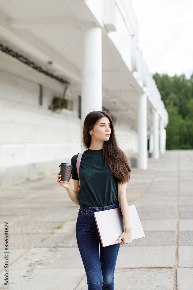 Beautiful young brunette woman carrying backpack and drinking takeaway coffee while walking outdoors Beautiful young brunette woman carrying backpack and drinking takeaway coffee while walking outdoors