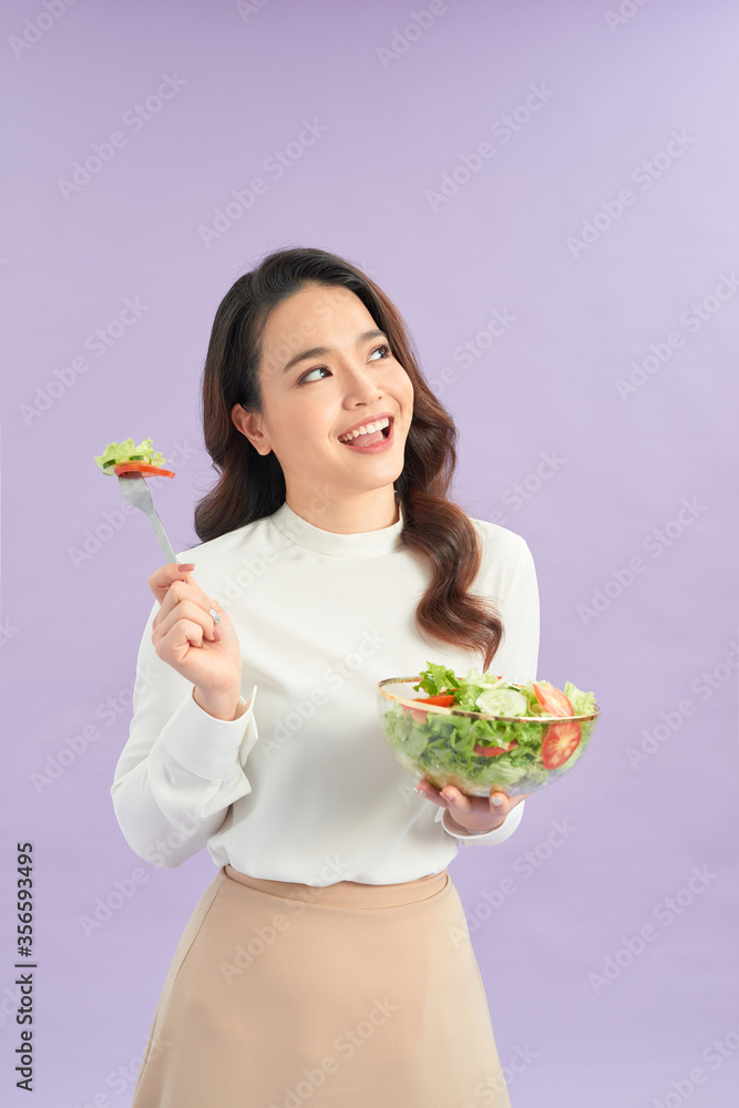 Portrait of a happy playful girl eating fresh salad from a bowl over purple background Portrait of a happy playful girl eating fresh salad from a bowl over purple background