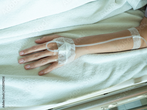 Portrait of tired female patient is lying and sleeping on the patient bed with the fluids on her hand in the wardroom at the hospital. Focus on the hand of the patient. White isolated background. photo