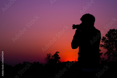 Photographer silhouette in outdoor taking a photograph in the sunset view landscape on top of a mountain with sunset twilight sky background. Color tone.