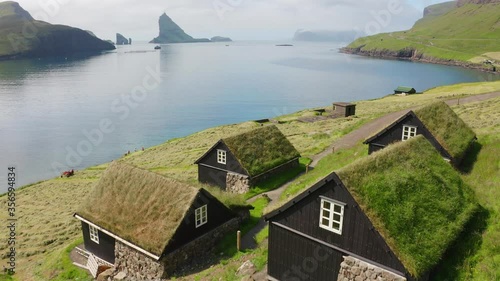 4k drone footage (Ultra High Definition). Captivating summer scene of Bour village with typical turf-top houses and Tindholmur cliffs on background. Aerial morning view of Vagar island, Faroe, Denmark photo