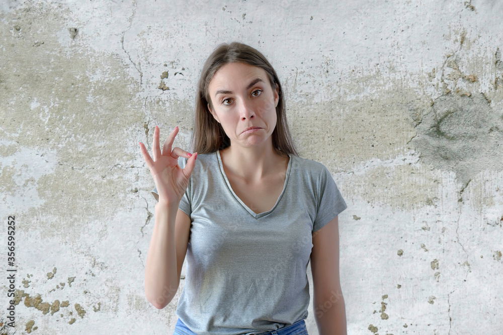 Woman showing ok sign with fingers digusted on a gray concrete background Woman showing ok sign with fingers digusted on a gray concrete background