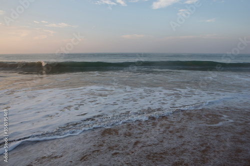 Beautiful seascape shot of the Indian ocean at sunrise with orange sand, a low tide with big white foamy waves and a blue orange sky on the horizon. Pitiwella beach, Sri Lanka