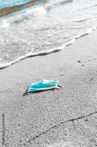 A blue face mask is left abandoned on the beach. It must be disposed in a proper hazardous waste bin, preventing germs spread. Corona Virus Covid19. Objects and medical supply. .