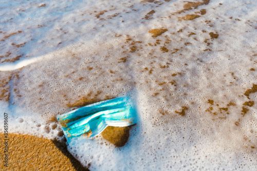 A blue face mask is left abandoned on the beach. It must be disposed in a proper hazardous waste bin, preventing germs spread. Corona Virus Covid19. Objects and medical supply. .