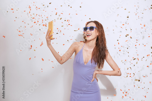 cheerful young girl in summer clothes taking a selfie under confetti rain