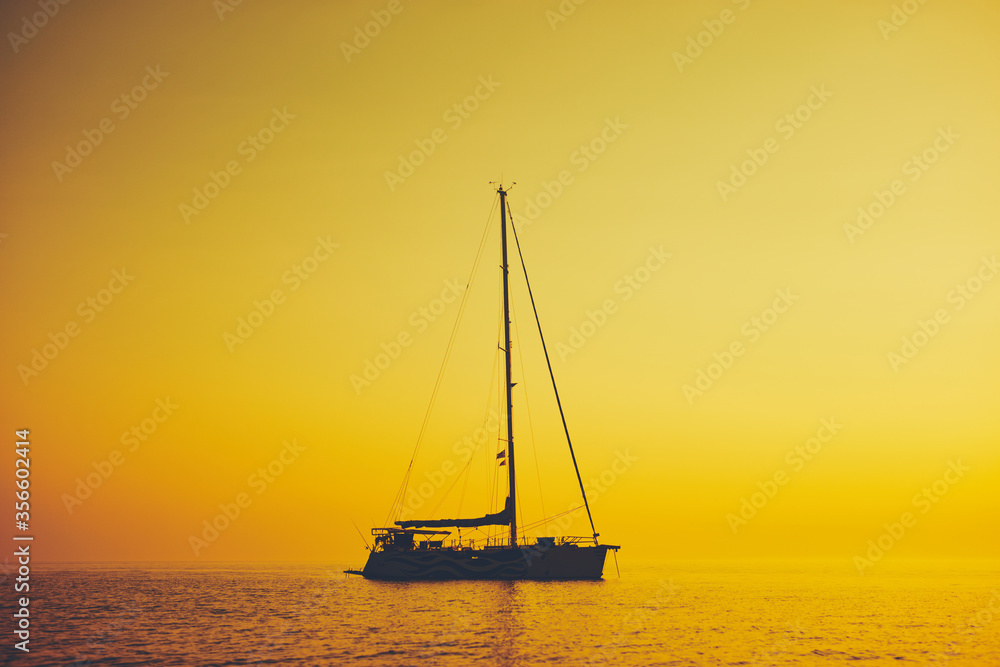 Silhouette of a sailing boat in sunset / sunrise time and ocean horizon.