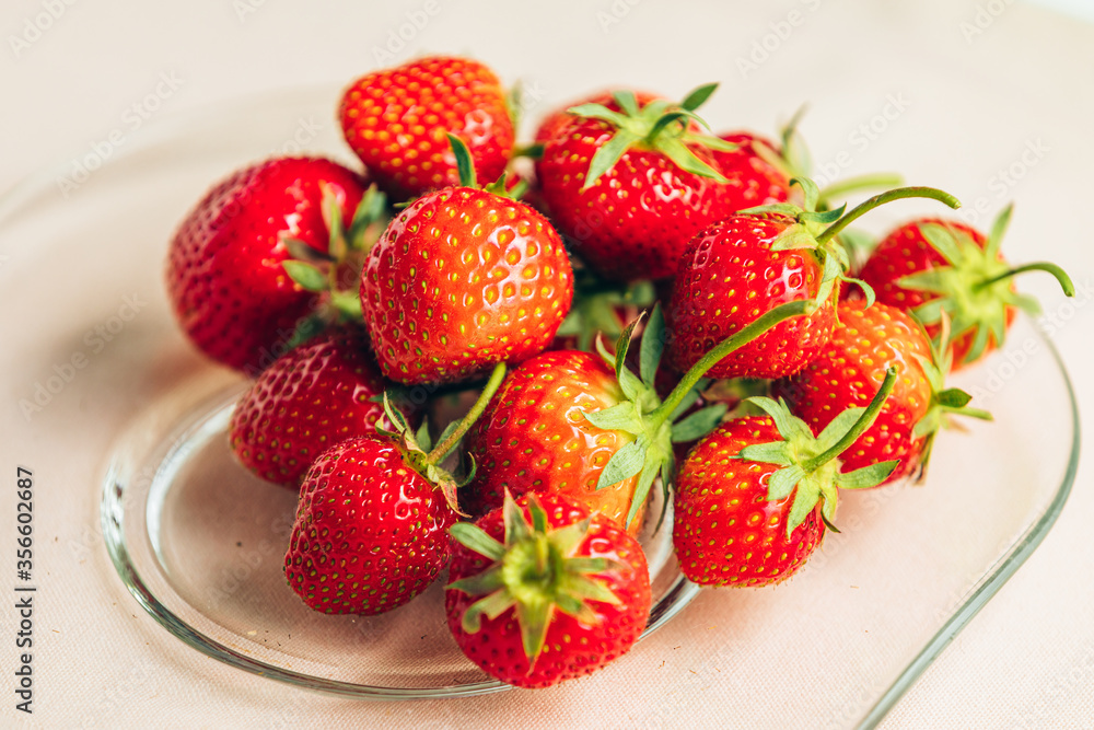 closeup ripe strawberries in a transparent glass dish on a pale pink background closeup ripe strawberries in a transparent glass dish on a pale pink background