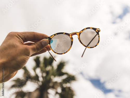 hand holding glasses with a palm and the sky as a background