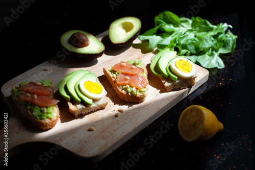 lemon and sandwiches with avocado, sliced egg, red fish and pine nuts on a wooden cutting board on the dark stone countertop