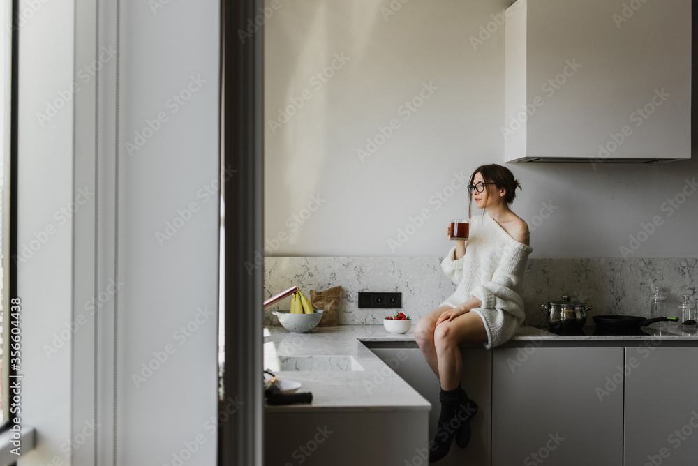 Beautiful woman in a sweater drinks coffee in the kitchen.