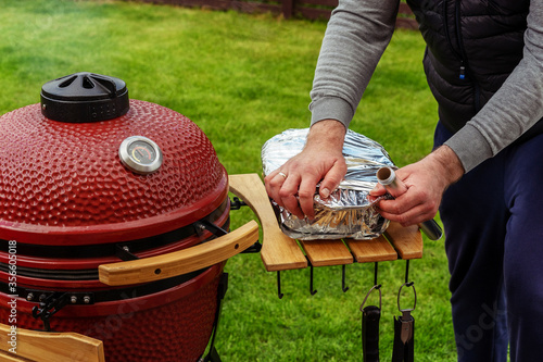 Red Ceramic Barbecue Grill. The man wraps the freshly prepared BBQ in foil.