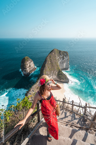 Wallpaper Mural A beautiful woman traveller wearing red dress and hat walking up from Kelingking beach in Nusa Penida island near Bali island in Indonesia Torontodigital.ca