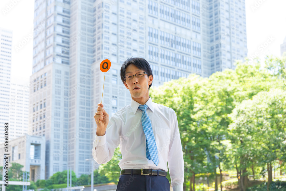 やせ型の真面目そうな日本人ビジネスマンがクエッションのボードを持っている