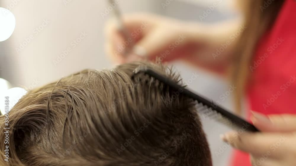 The girl the hairdresser cuts hair with scissors and a comb does a