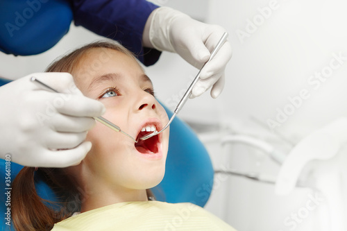 Doctor examining little european girl sitting at dental chair. Pediatric dentistry.