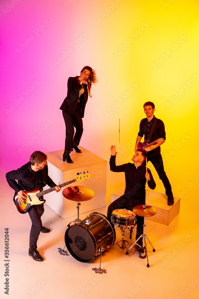Fototapeta premium Young and joyful caucasian musicians performing on gradient studio background in neon light. Concept of music, hobby, festival. Colorful portrait of modern artist. Inspiring. Art, cover band. Top view
