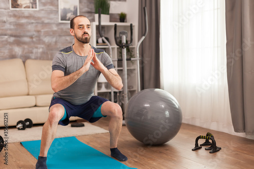 Athletic man doing squats for legs during self isolation. photo