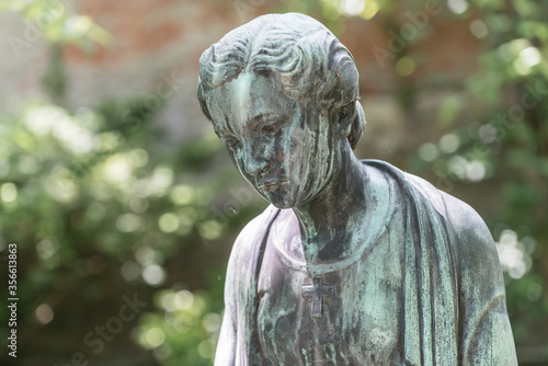 Nahaufnahme einer weiblichen Bronzestatue Frau mit kurzen Haaren mit Kreuz und Strickjacke in einem Park, Deutschland photo