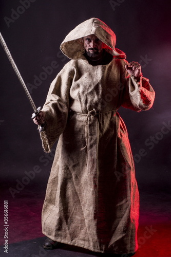 фотографія A monk Inquisitor in a cassock with chains and a flaming sword on a black background