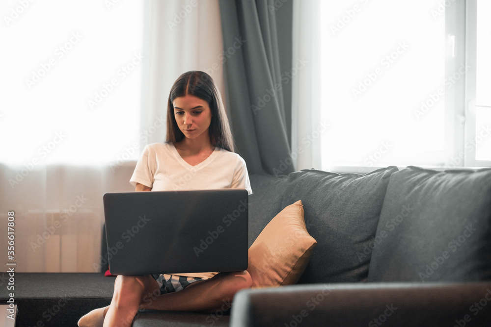 Young woman with modern laptop sitting on sofa at home Young woman with modern laptop sitting on sofa at home