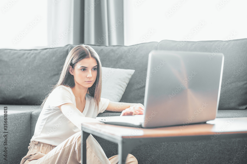 Fototapeta premium Young woman with modern laptop sitting on sofa at home