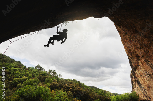 Silhouette of a young man climbing a collapsed wall inside a cave. Cloudy sky background.