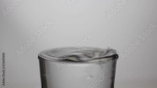 Drops of water falling into a glass full of water; pure and transparent water; drip, drop by drop