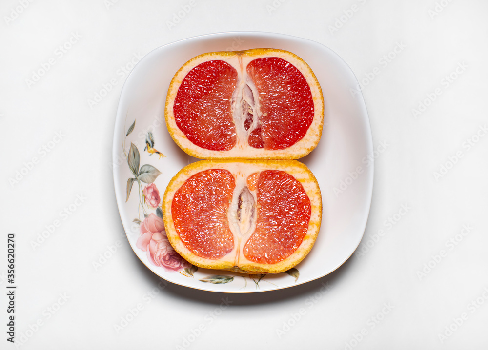 photo of the inside of two halves of the same pink grapefruit lying in a light plate on a light background.