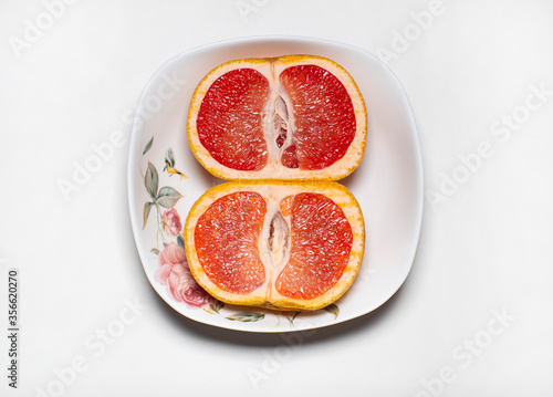 photo of the inside of two halves of the same pink grapefruit lying in a light plate on a light background.