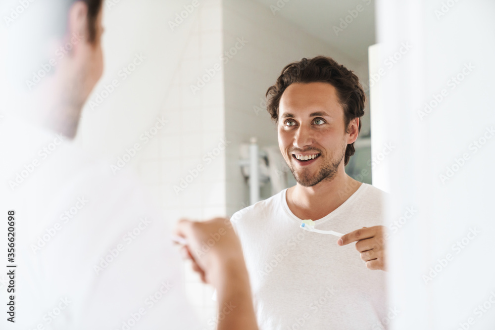 Attractive young man standing in front of the bathroom mirror Attractive young man standing in front of the bathroom mirror