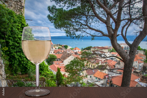 Glass of wine on sea blur background and old Mediterranean town Omis in Croatia. Red rooftops of historic old town.