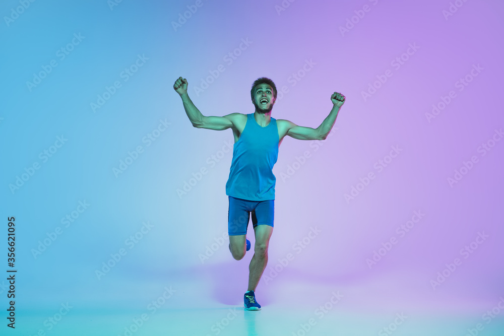 The first. Portrait of young caucasian man running, jogging on gradient studio background in neon light. Professional sportsman training in action and motion. Sport, wellness, activity, vitality The first. Portrait of young caucasian man running, jogging on gradient studio background in neon light. Professional sportsman training in action and motion. Sport, wellness, activity, vitality