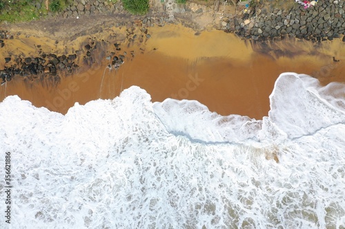 aerial drone bird view shot of the sea shore with yellow sand, black rocks, large white waves and foam crashing on the beach forming beautiful textures, patterns, shapes. Sri Lanka photo