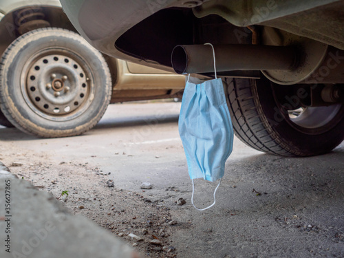 Photography A medical mask hangs on the exhaust pipe of a car