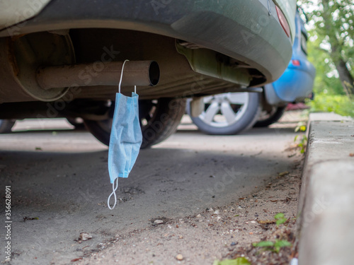 A medical mask hangs on the exhaust pipe of a car. The concept of environmental pollution by harmful toxic emissions provoking serious diseases.