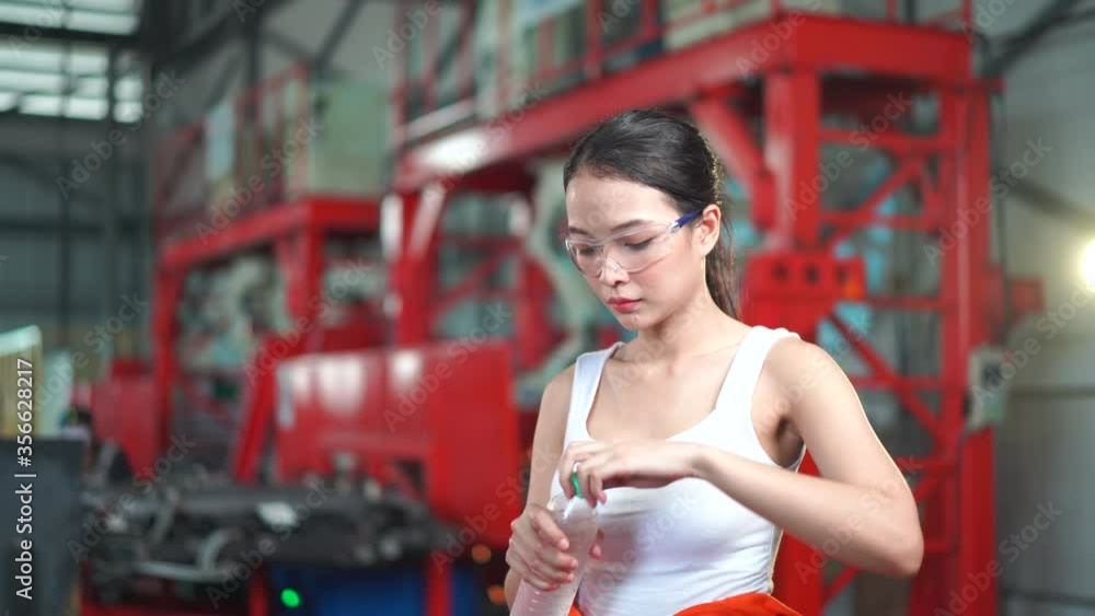 Young Asian female worker drinks water at welding steel industrial factory. Young Asian female worker drinks water at welding steel industrial factory.