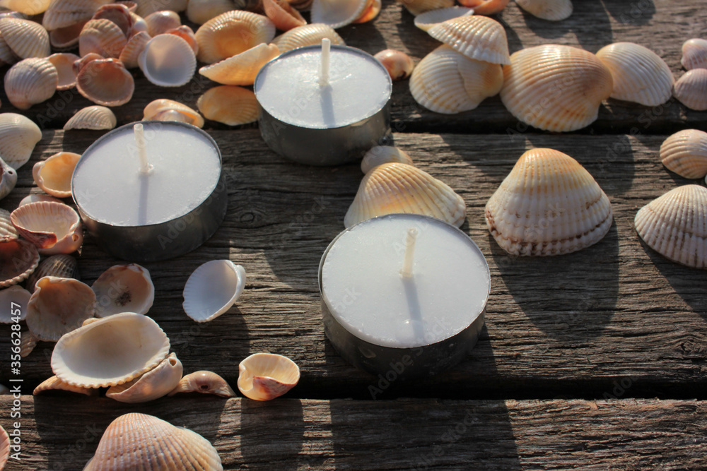 Tea candles and seashells on the beach wooden pier. Summer romantic evening
