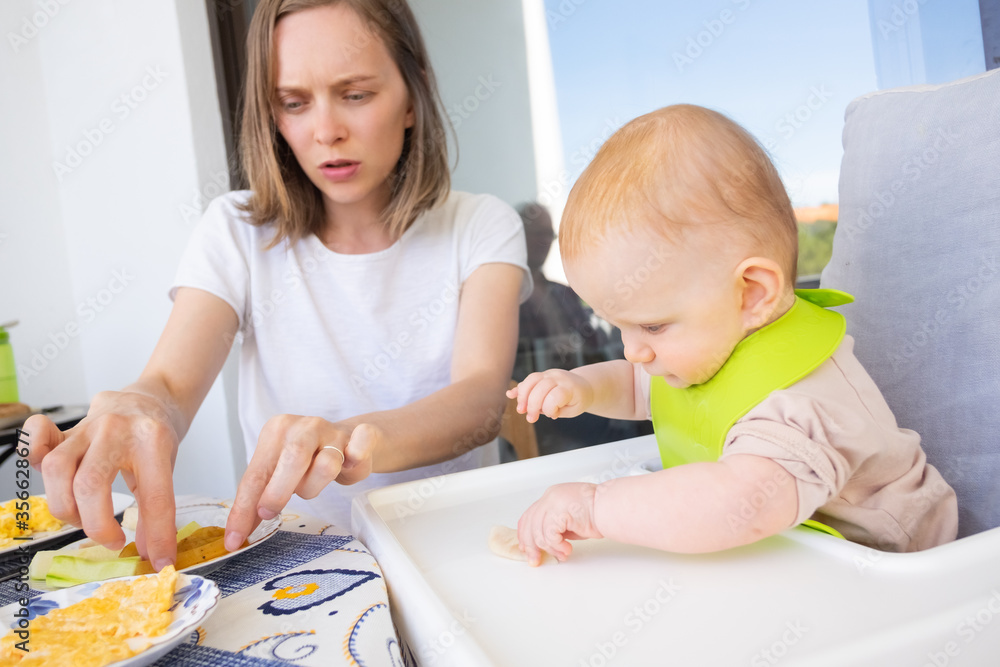 Mom feeding baby daughter with slices of fruits and vegetables. First solid food or child care at home concept Mom feeding baby daughter with slices of fruits and vegetables. First solid food or child care at home concept