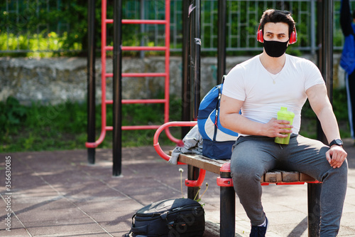 Portrait sports arabian man in black medical face mask posed outdoor with earphones during coronavirus quarantine.