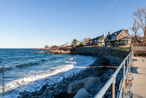 Rockport, Massachusets / USA - 02.15.2020 Beautiful wooden covered, white-colored houses on the bank of Atlantic ocean with crashing waves and rocks on the foreground
