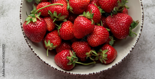 Close up top view of fresh ripe organic strawberry in ceramic  bowl on light gray background. Organic fruit diet. Healthy vegetarian nutrition