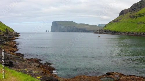 Lonely yacht on the Atlantic coast, Tjornuvik public beach. Wonderful morning scene of Streymoy island with Eidiskollur cliffs on background, Faroe Islands, Denmark. 4K video (Ultra High Definition). photo