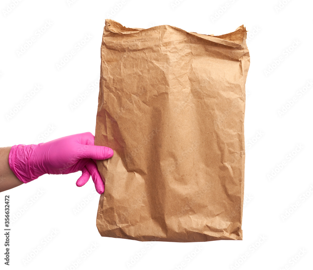 hand in a pink latex glove holds a full paper bag of brown craft paper, concept of remote and contactless food delivery hand in a pink latex glove holds a full paper bag of brown craft paper, concept of remote and contactless food delivery