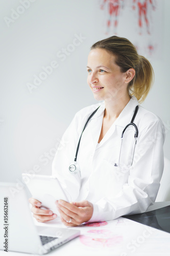 young, attractive blonde doctor is sitting in her office, working on her tablet and looking at examination results