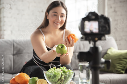 Smiling. Caucasian blogger  woman make vlog how to diet and lost weight  be body positive  healthy eating. Using camera recording her fruits salad preparing. Lifestyle influencer  wellness concept.