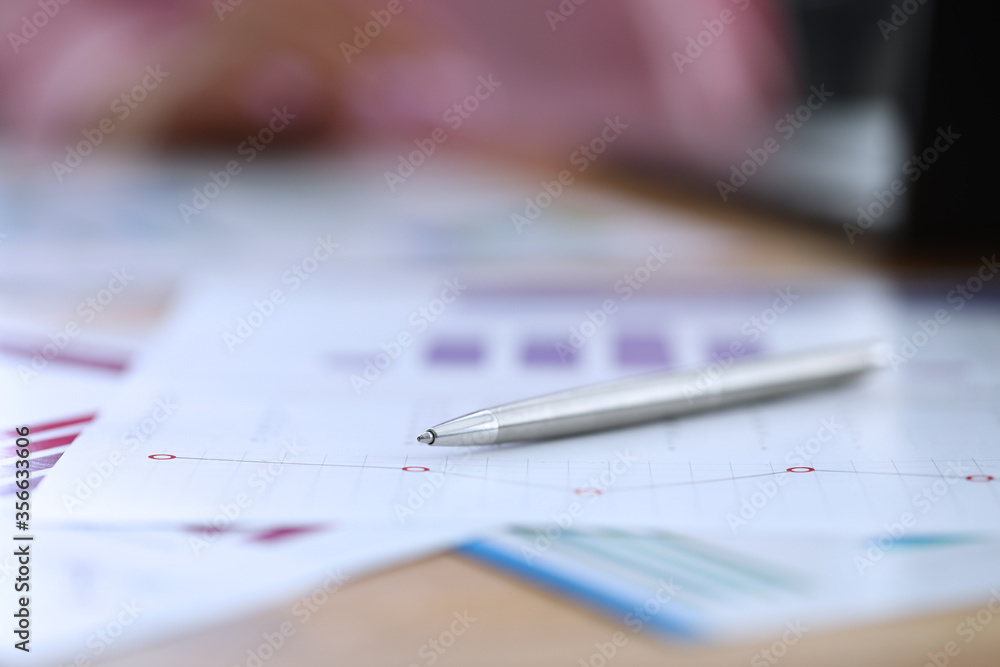 Close-up of silver pen laying on business papers. Working desktop with documents. Diagrams and graphs. Financial company. Statistics report. Economy and finance concept Close-up of silver pen laying on business papers. Working desktop with documents. Diagrams and graphs. Financial company. Statistics report. Economy and finance concept
