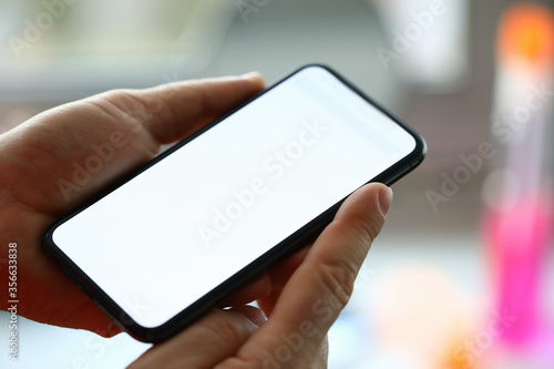 Close-up of person holding modern smartphone with white screen. Adult using mobile phone for searching information. Text on display. Technology and spare time concept