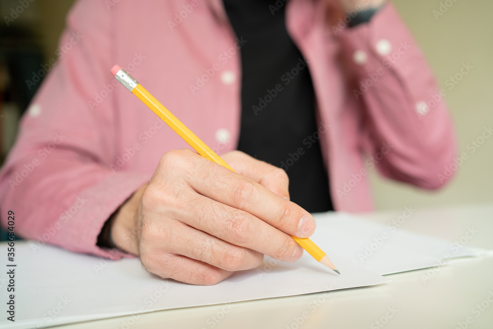 Hand holding pencil and drawing on paper. Unrecognizable guy in pink shirt making notes and sitting on isolation. Working at home and freelance concept Hand holding pencil and drawing on paper. Unrecognizable guy in pink shirt making notes and sitting on isolation. Working at home and freelance concept